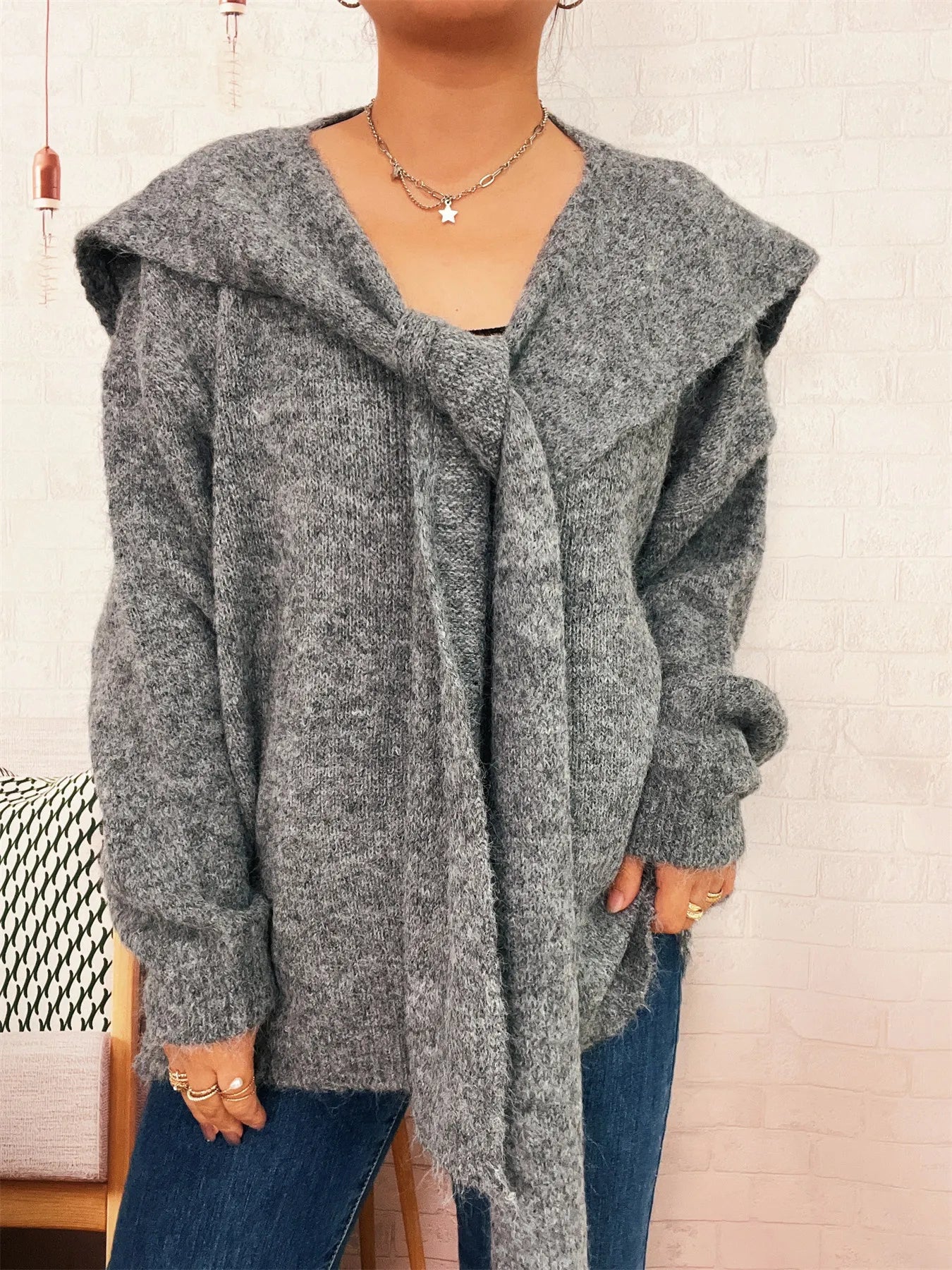 Person wearing a gray hooded cardigan with a neutral background