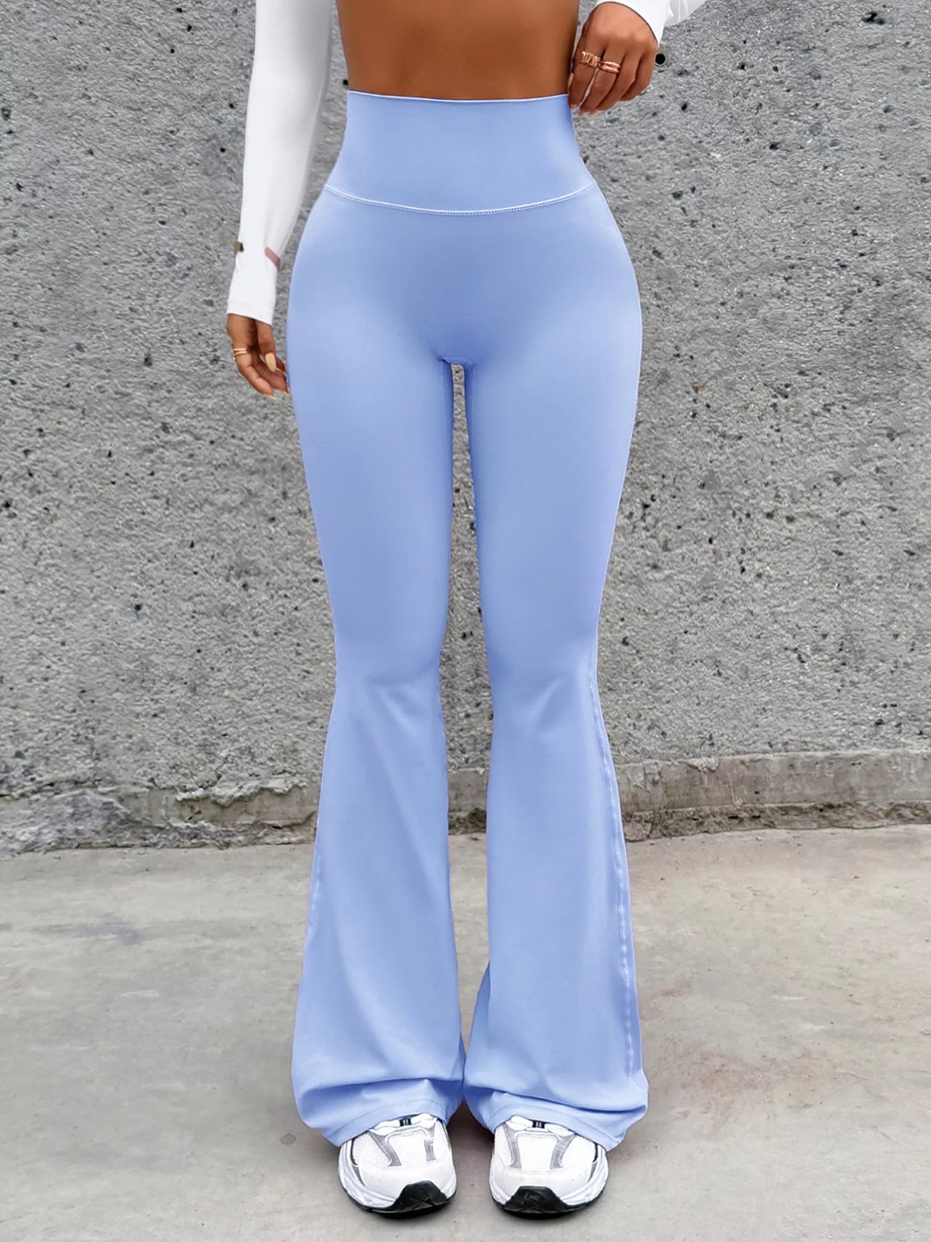 Person wearing light blue flared pants against a gray concrete wall.