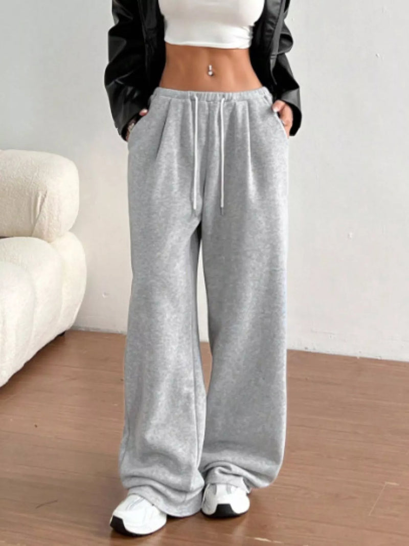 Person wearing gray sweatpants with a white top and black jacket in a minimalistic room.