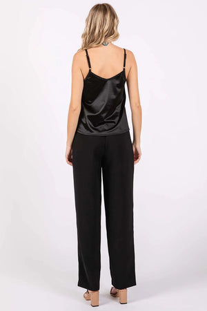 Woman wearing a black satin camisole and black pants on a white background