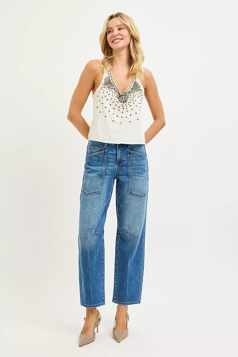 Woman wearing a white sleeveless top with embellishments and blue jeans on a white background