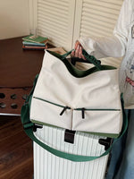 White bag with green accents held by a person over a white suitcase.