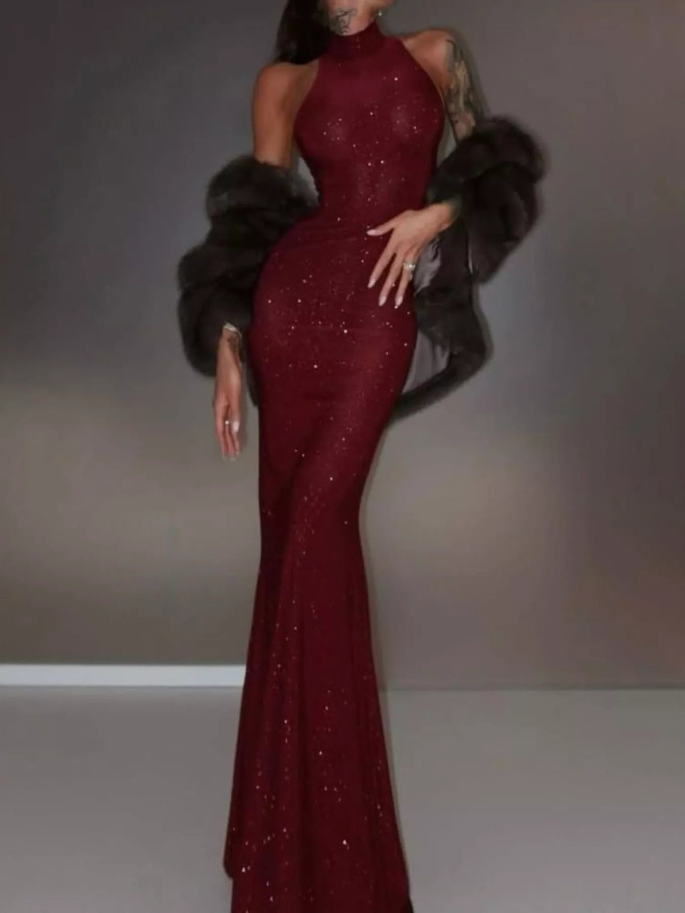 Woman wearing a burgundy evening gown with a fur stole against a neutral background
