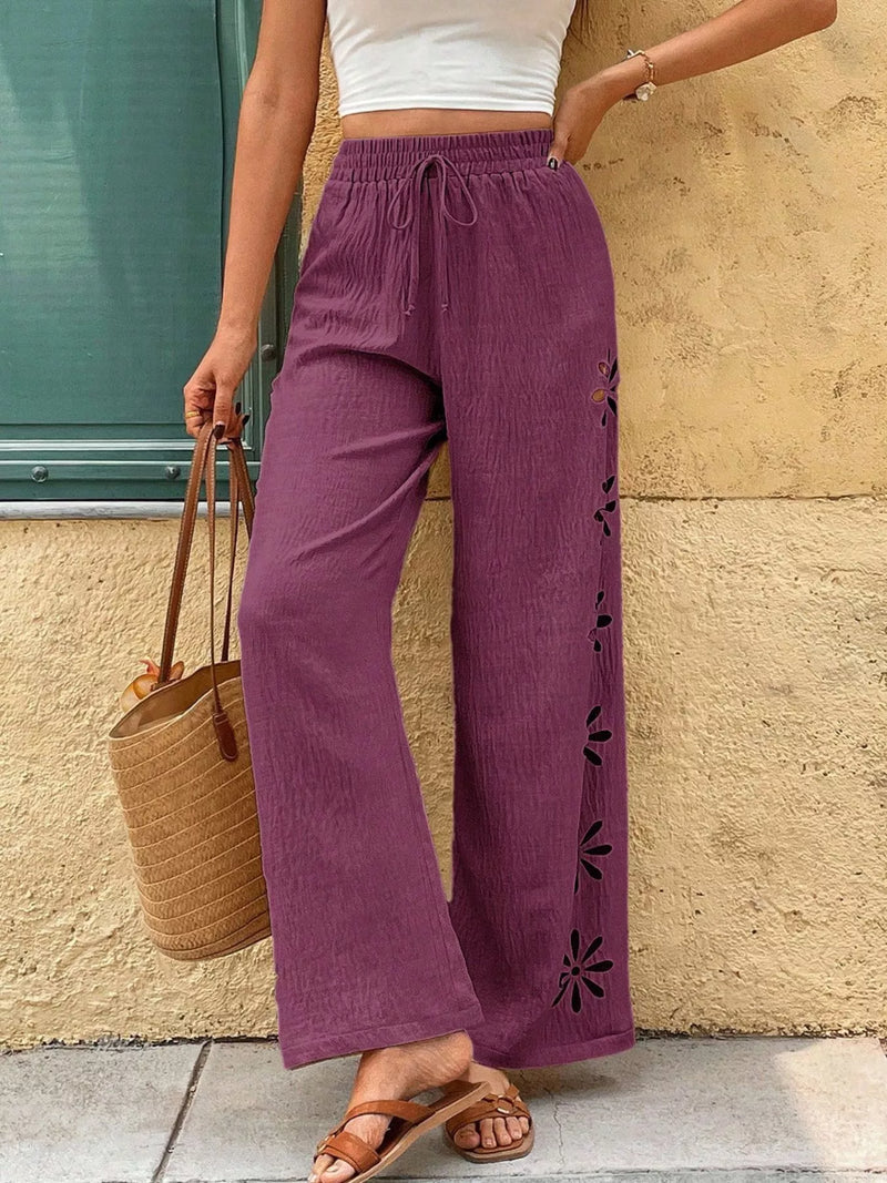 Person wearing purple pants with floral cut-out details against a beige wall.