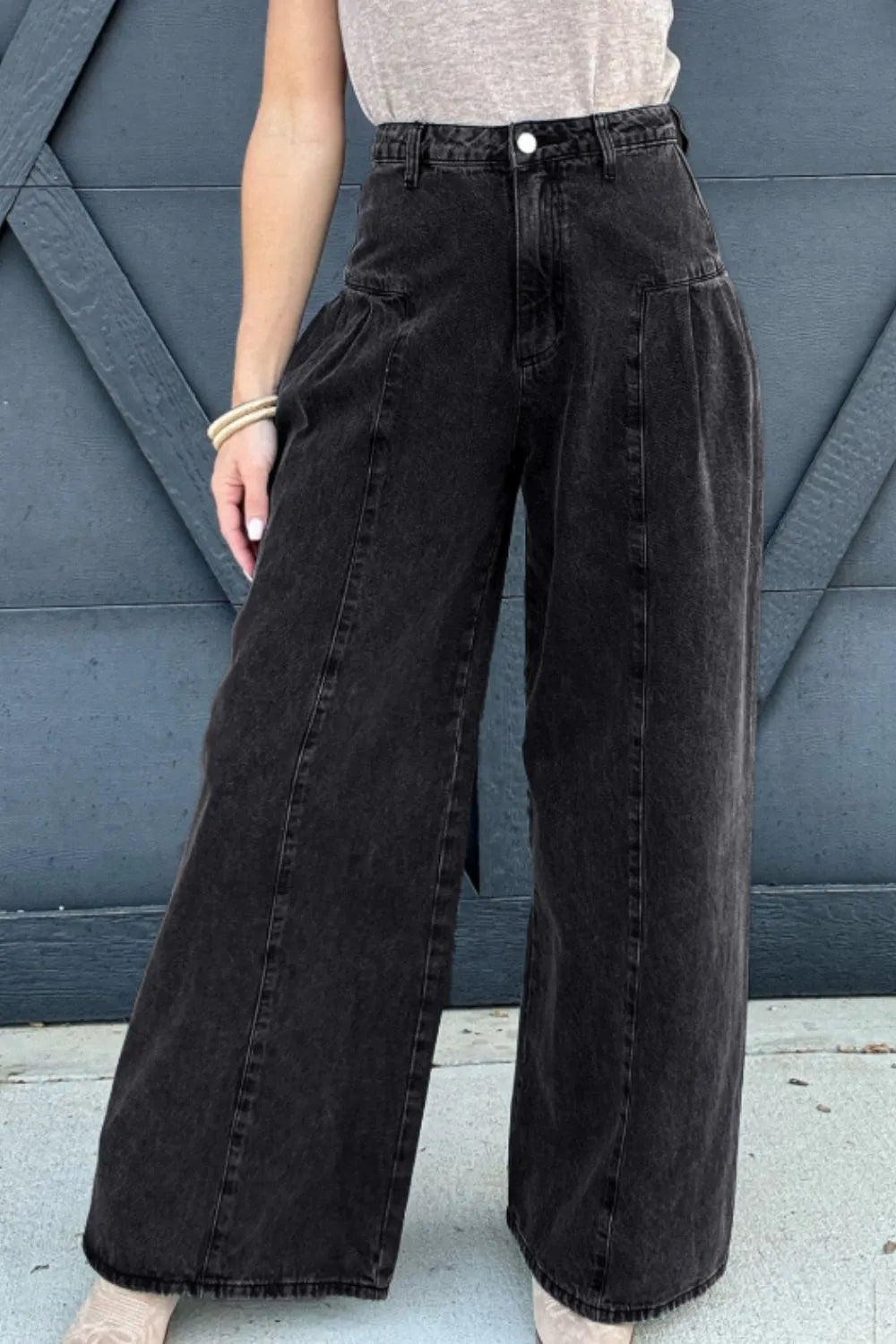 Person wearing black wide-leg jeans against a blue wall.