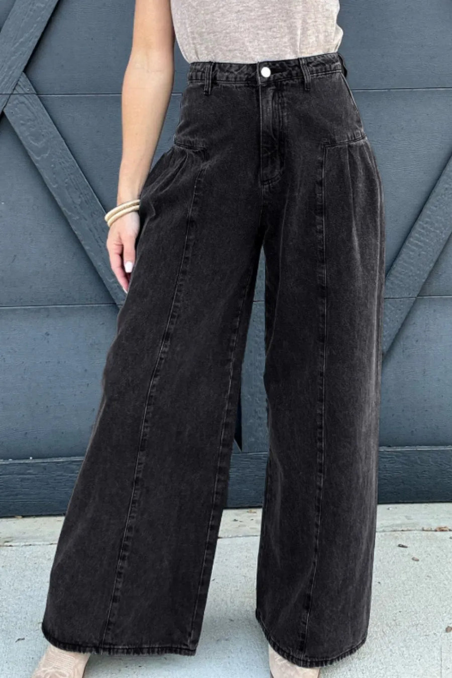 Person wearing black wide-leg jeans against a blue wall.