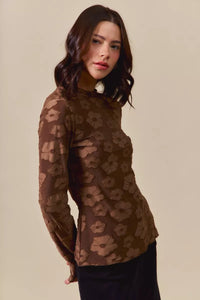 Woman wearing a brown floral patterned top against a beige background