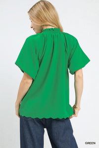 Woman wearing a green blouse with scalloped hem on a white background