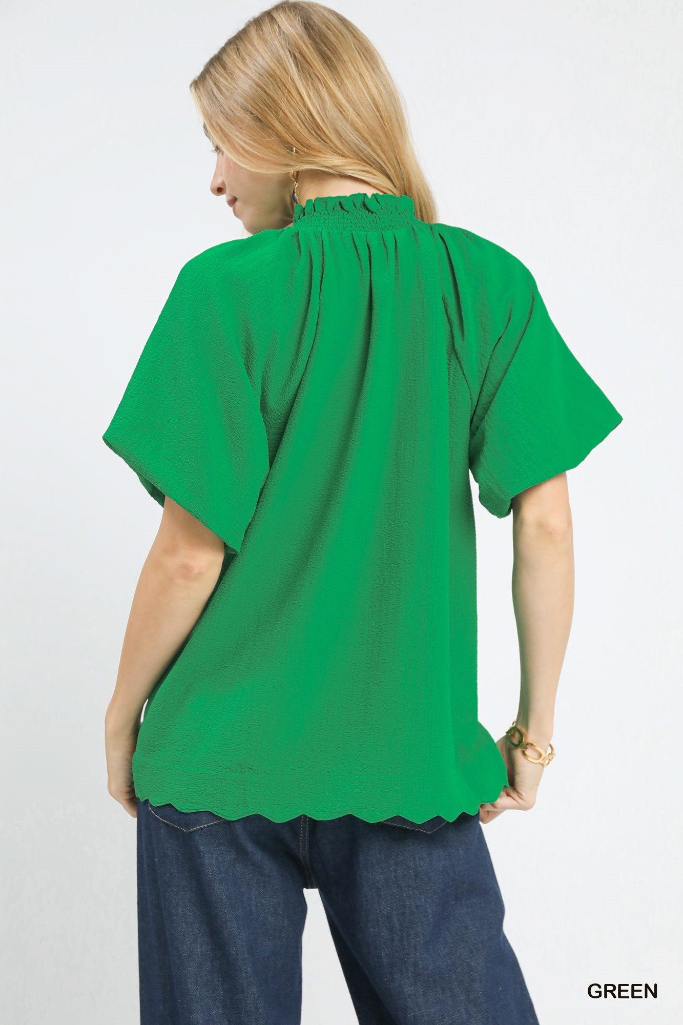 Woman wearing a green blouse with scalloped hem on a white background