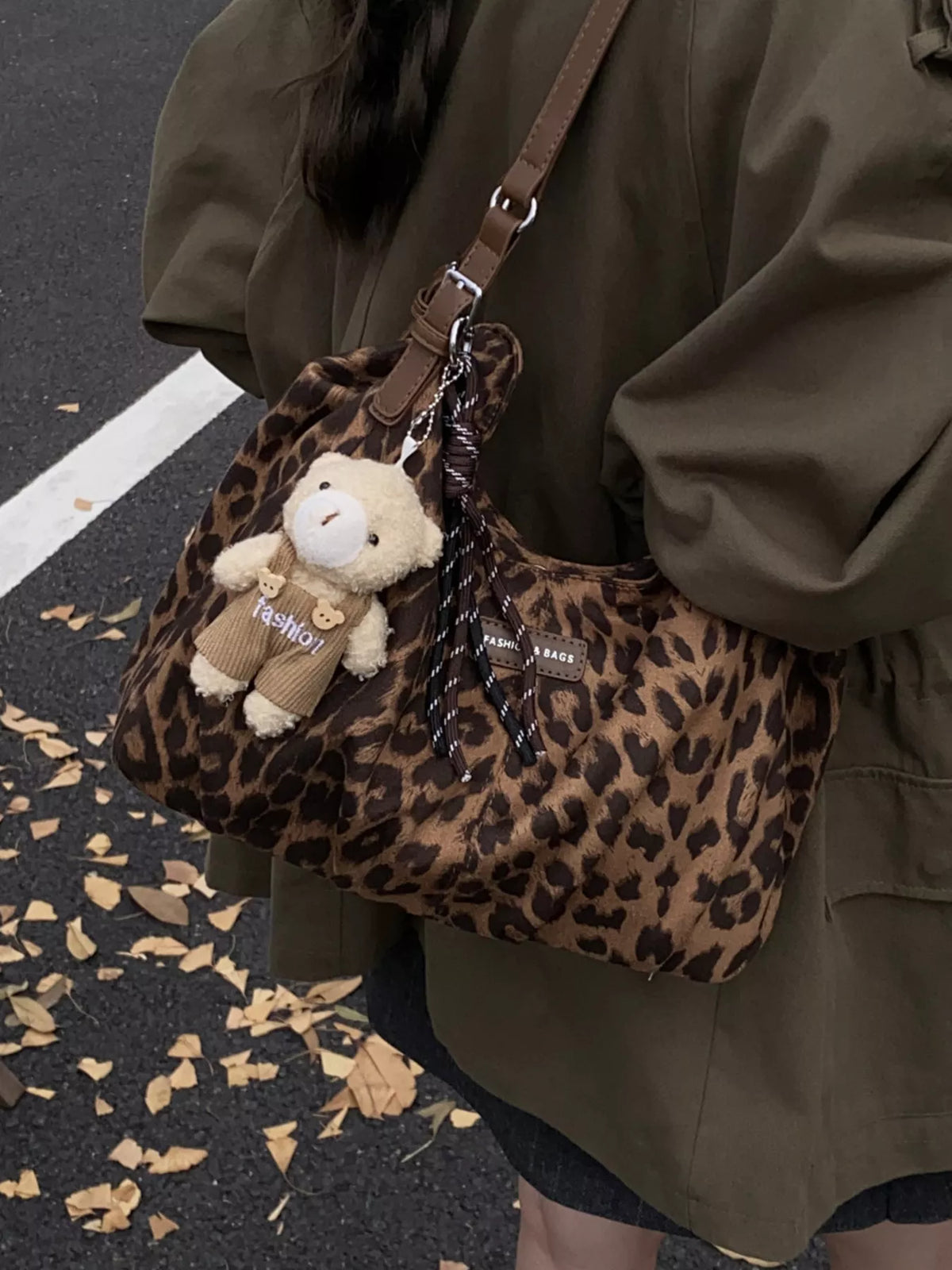 Person holding a leopard print handbag with a teddy bear charm on a street.