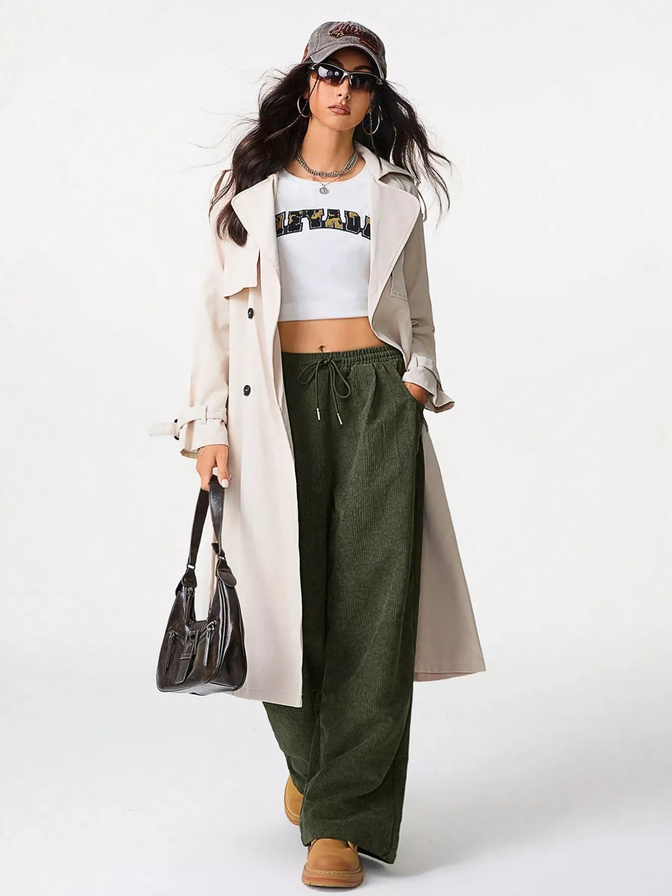 Woman wearing a white trench coat, green pants, and a cap on a white background