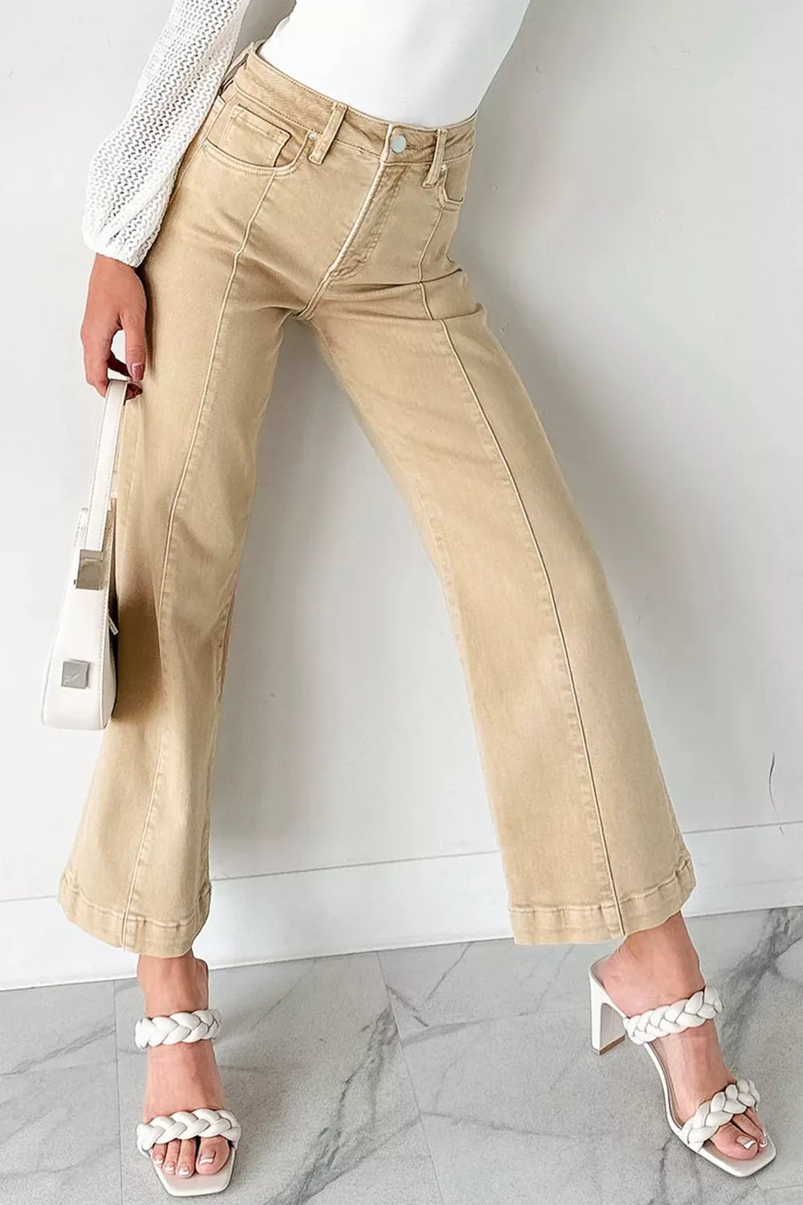 Person wearing beige pants and white sandals on a marble floor with a white wall background