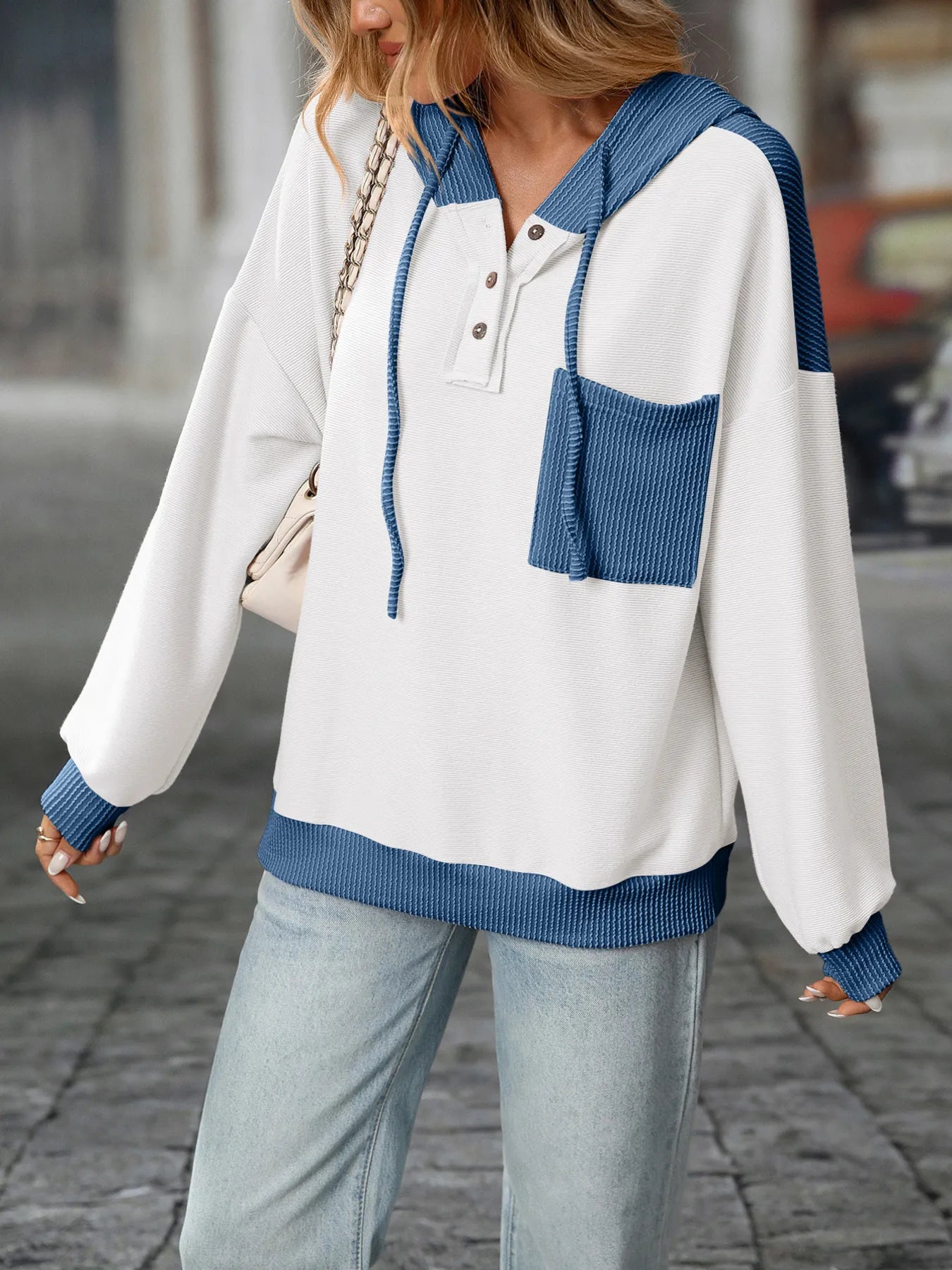 Person wearing a white and blue sweater with a hood on a blurred street background