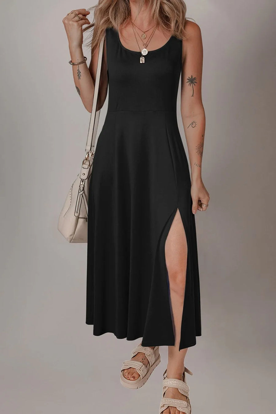 Woman wearing a black dress with a slit, standing against a plain background