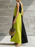 Woman wearing a black and green dress holding a patterned handbag against a stone wall.