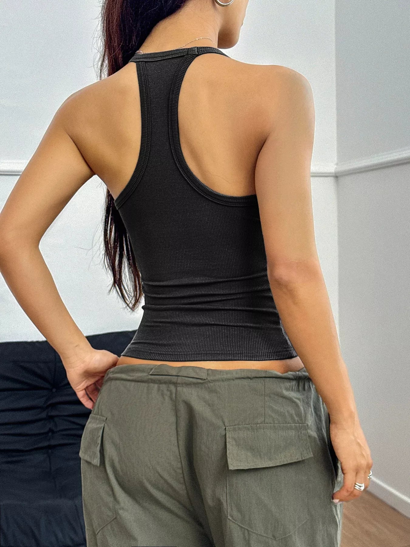 Person wearing a black tank top and green cargo pants against a white wall.