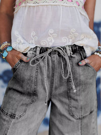 Person wearing a white embroidered top and gray wide-leg jeans with a blurred background