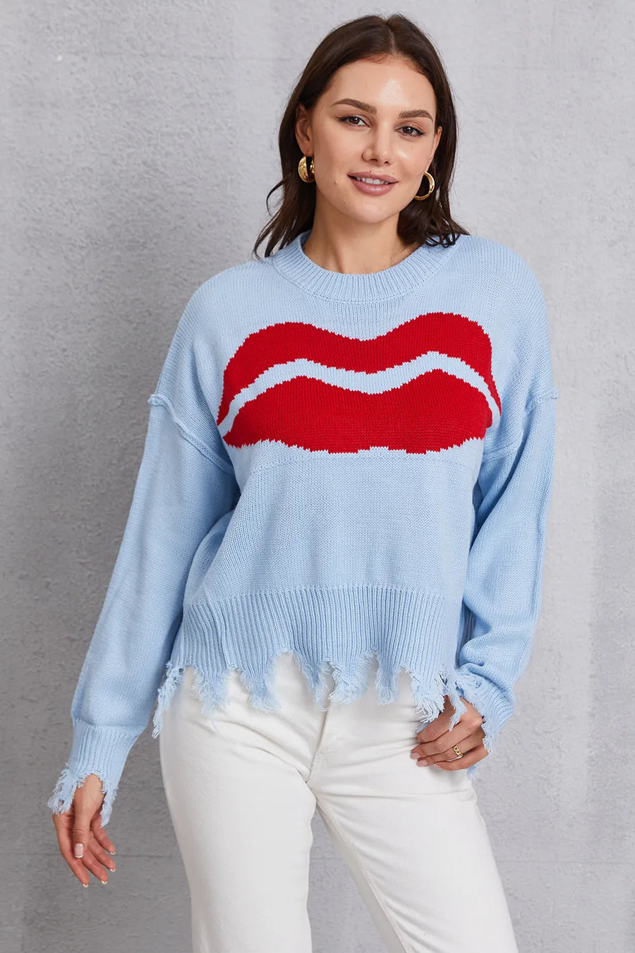 Woman wearing a light blue sweater with a red and white design, standing against a gray background