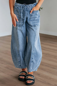 Person wearing wide-leg blue jeans on a wooden floor.