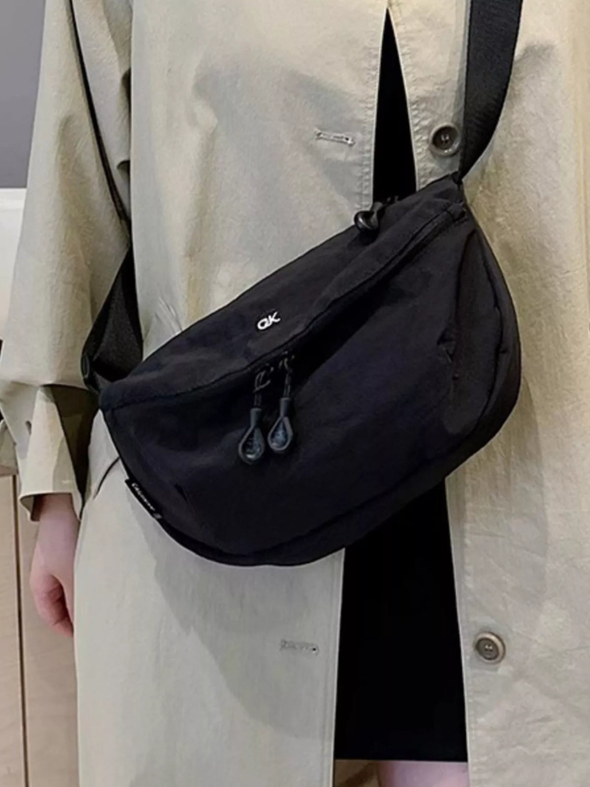 Person wearing a black shoulder bag with a visible brand logo.