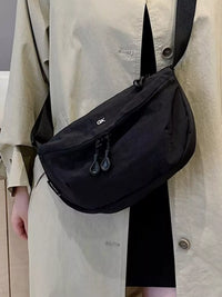 Person wearing a black shoulder bag with a visible brand logo.