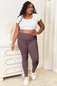 Woman wearing a white crop top and dark gray leggings standing in a room with a white dresser.
