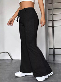 Person wearing black flared pants and white sneakers in a minimal indoor setting