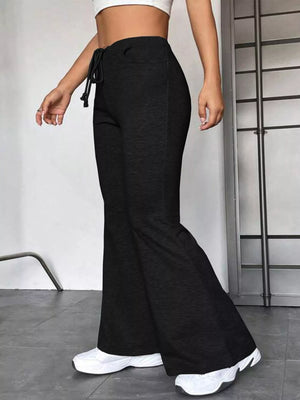 Person wearing black flared pants and white sneakers in a minimal indoor setting