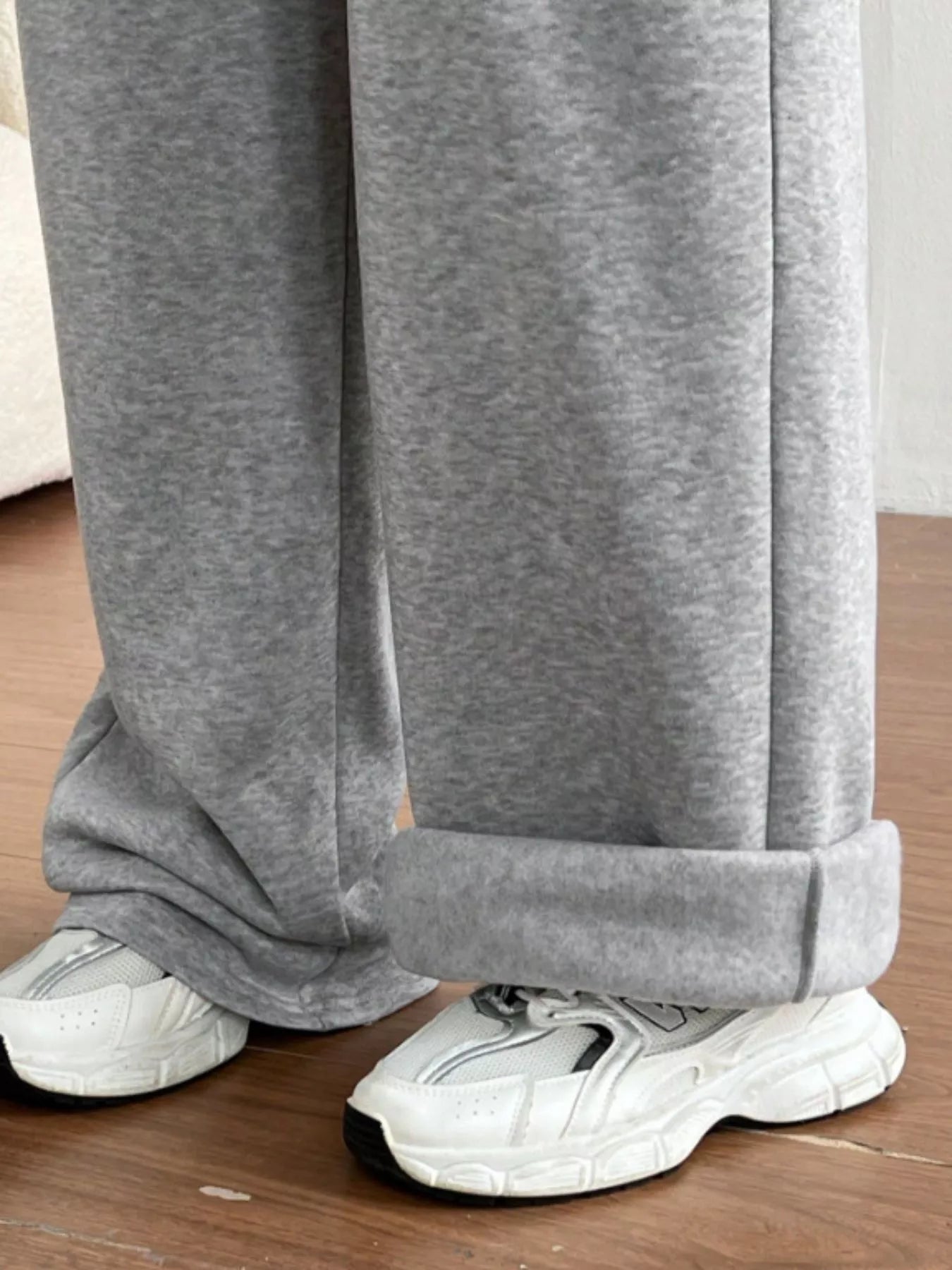 Gray sweatpants being worn with white sneakers on a wooden floor.