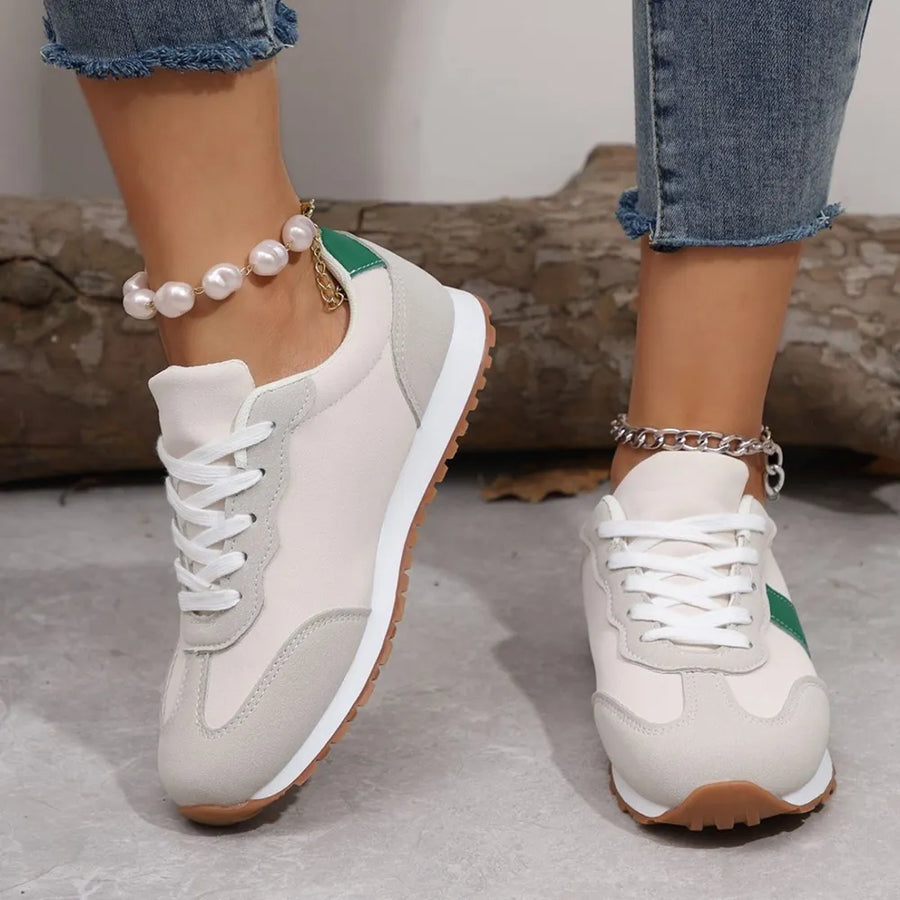 White sneakers with brown soles worn by a person, with a neutral background.