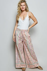 Woman wearing a white top and floral pants against a gray background