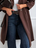 Person wearing a brown coat and blue jeans against a white background