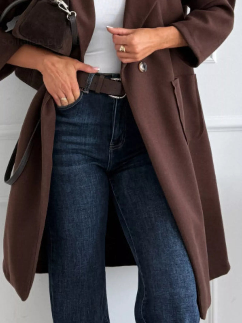 Person wearing a brown coat and blue jeans against a white background