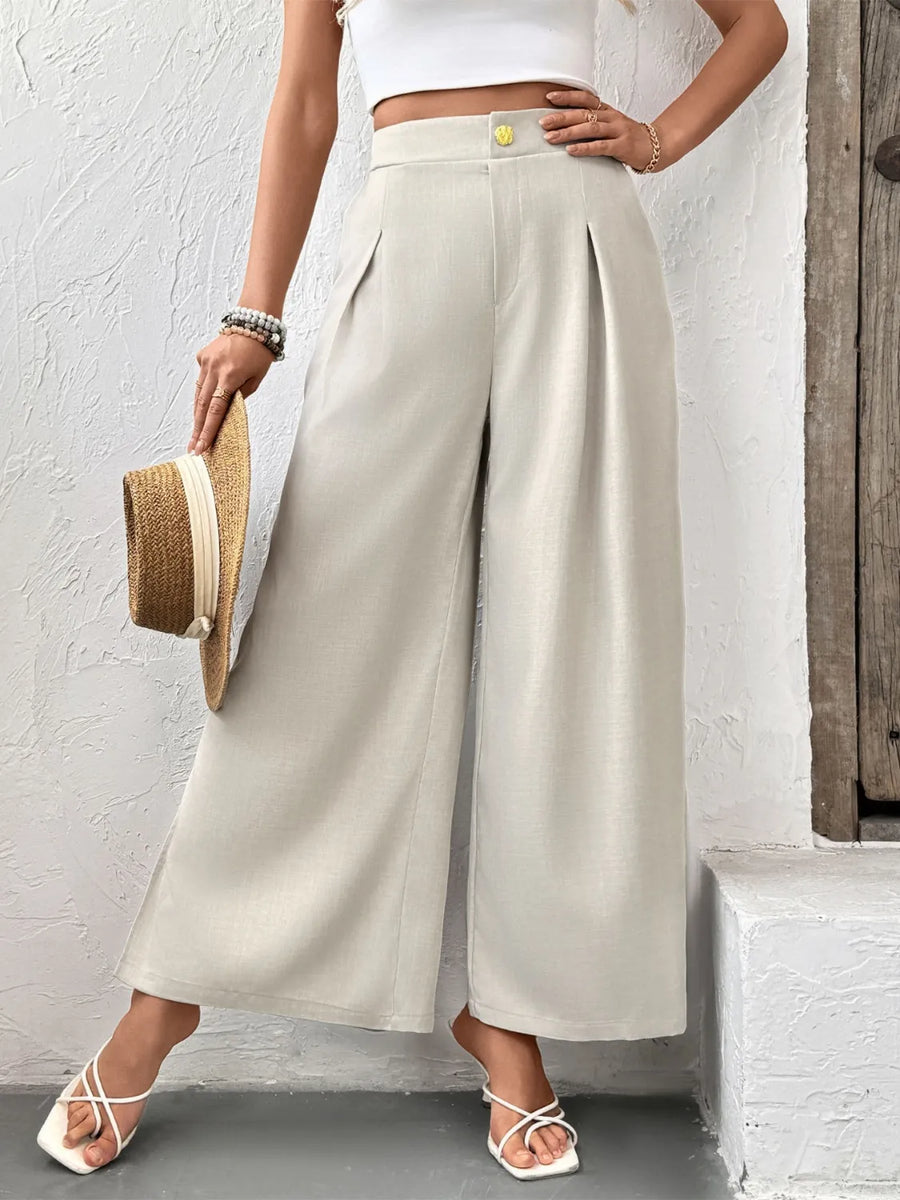 Person wearing beige wide-leg pants and white top against a light gray wall.