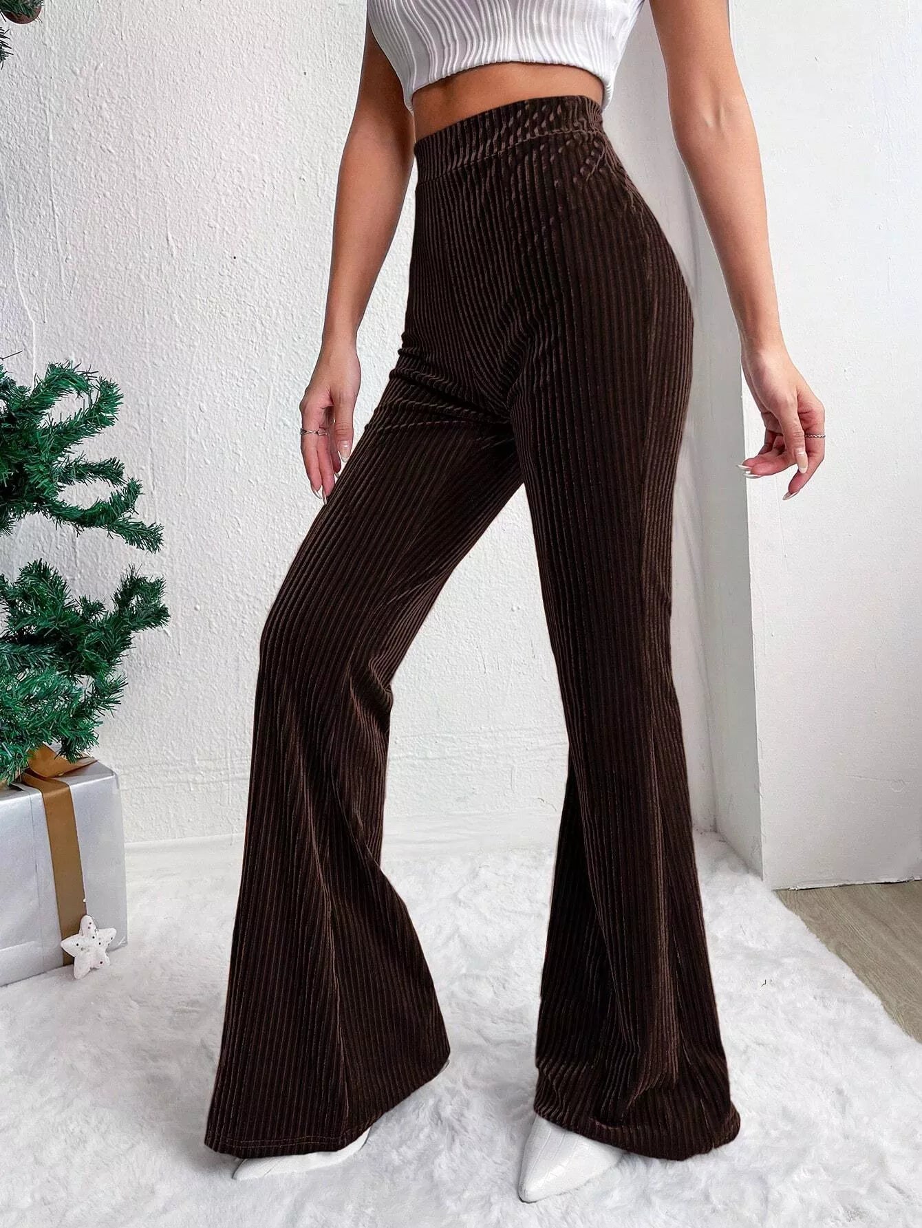 Brown pleated flared pants worn by a person on a white background