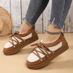 Brown and white sneakers with thick soles worn by a person on a wooden floor.
