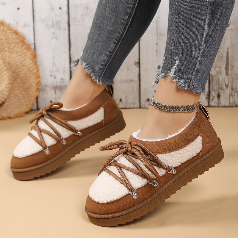 Brown and white sneakers with thick soles worn by a person on a wooden floor.