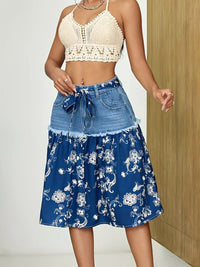 Woman wearing a white lace top and blue floral skirt against a neutral background
