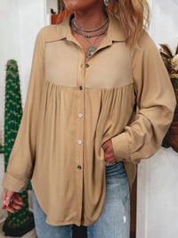 Person wearing a beige button-up shirt and blue jeans indoors.
