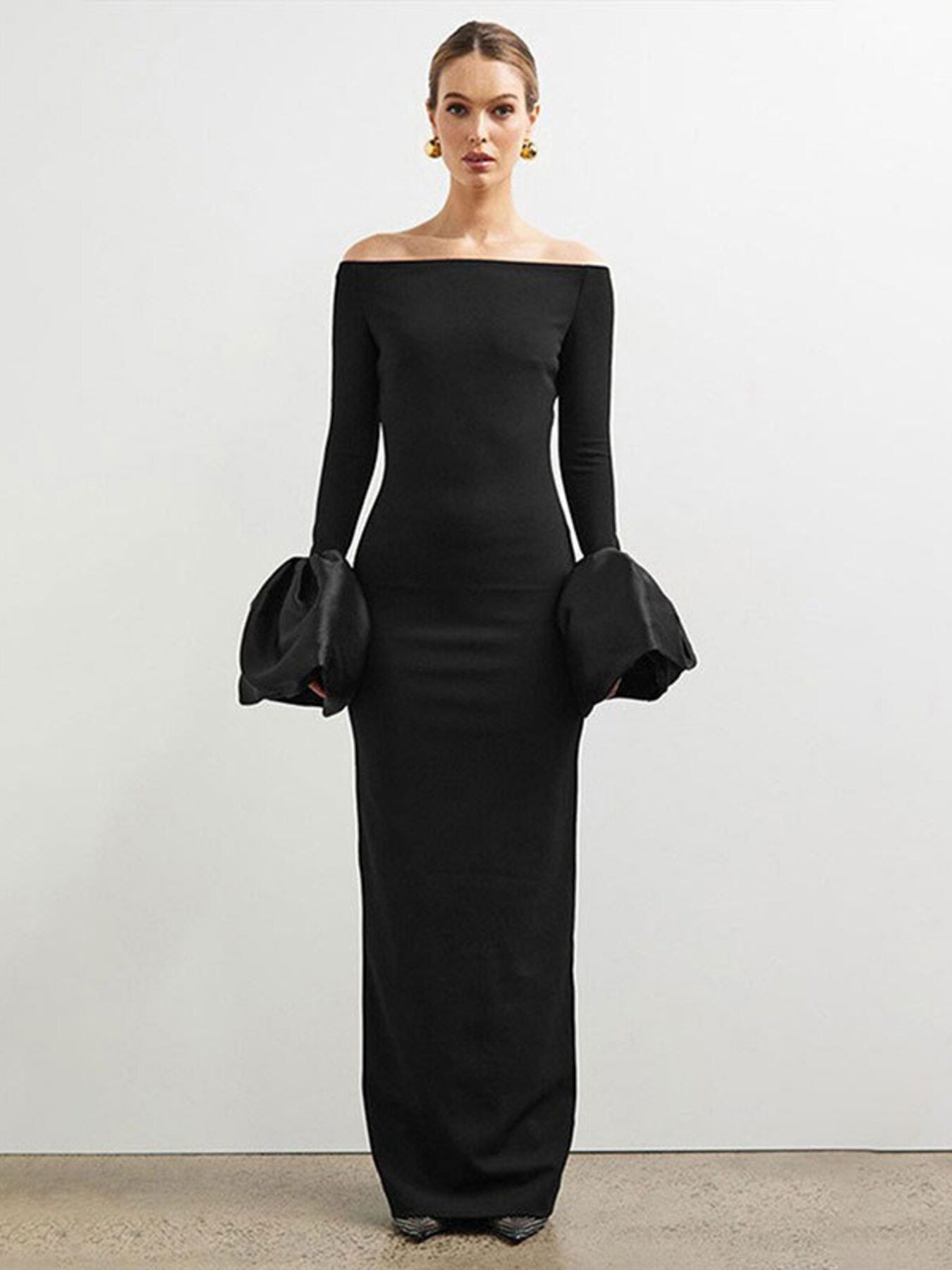 Woman wearing a black off-shoulder gown with long sleeves against a plain background