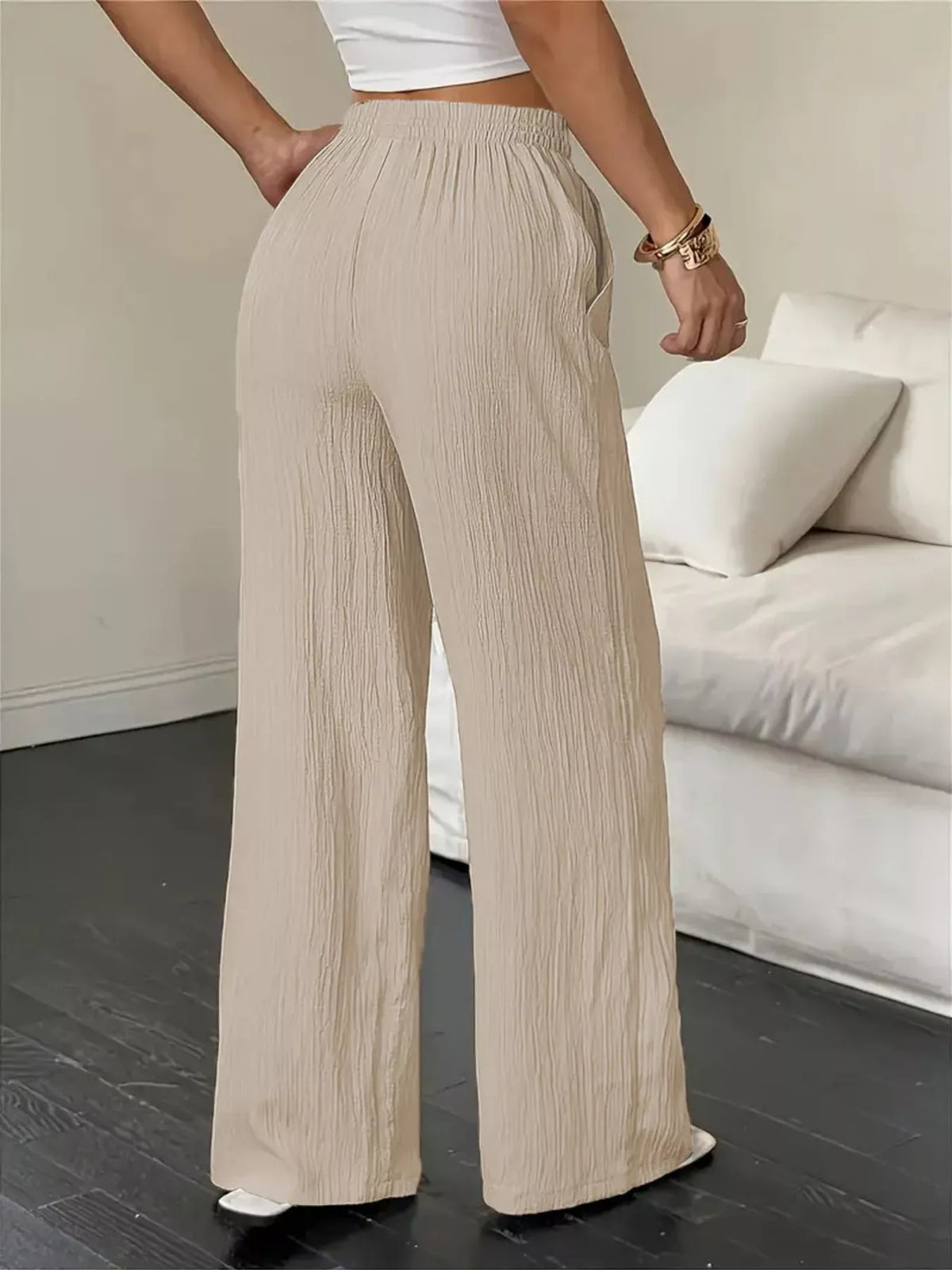 Person wearing beige pleated pants in a minimalistic room with a white couch.