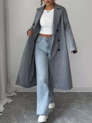 Person wearing a long gray coat, white top, and light blue jeans on a plain background