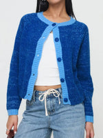 Person wearing a blue knitted cardigan over a white top and jeans on a plain background
