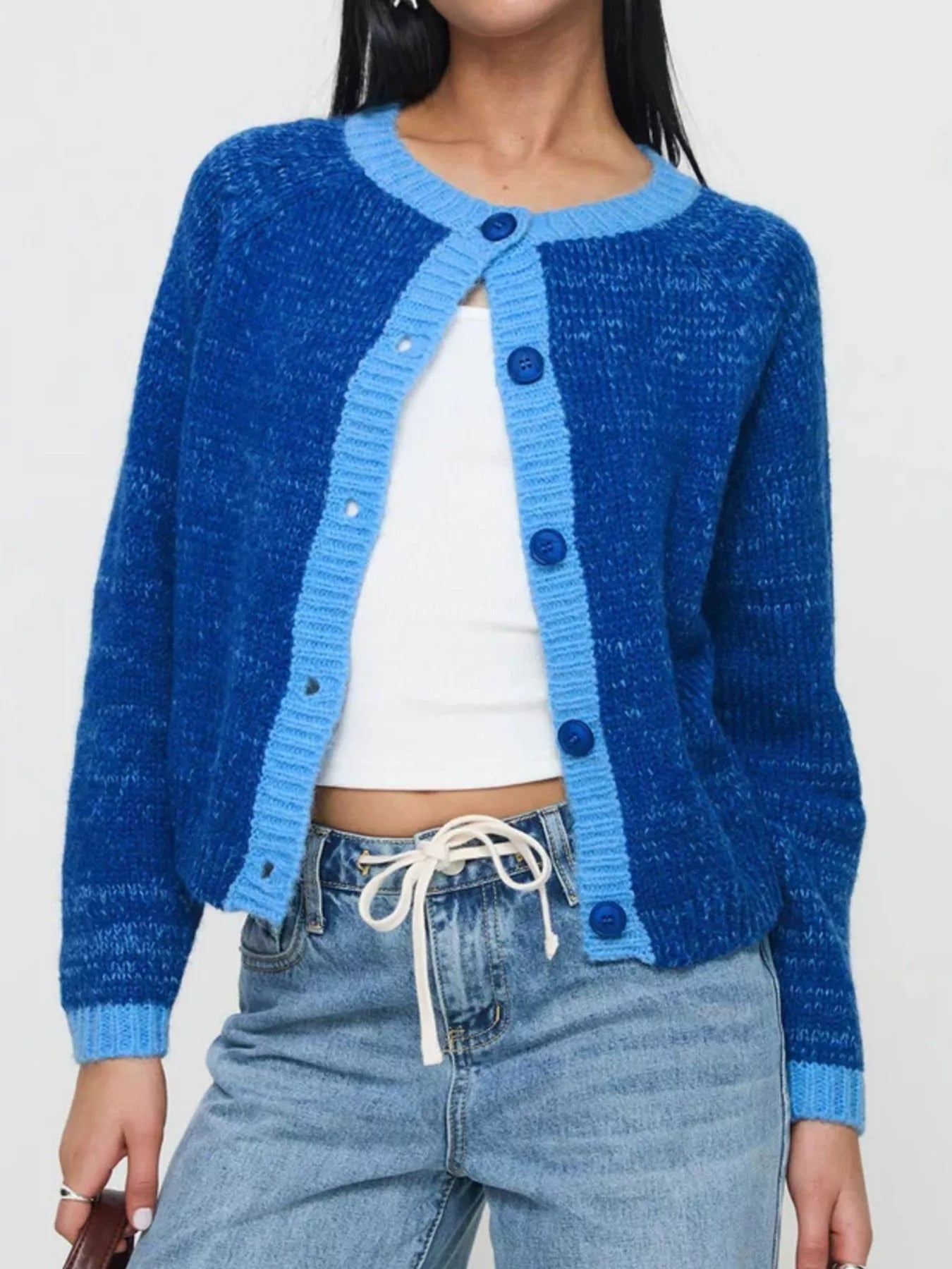 Person wearing a blue knitted cardigan over a white top and jeans on a plain background
