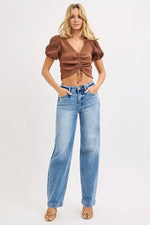 Woman wearing a brown top and blue jeans on a white background