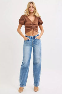 Woman wearing a brown top and blue jeans on a white background