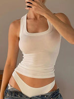 Person wearing a white tank top and denim shorts against a plain background