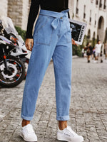 Person wearing blue jeans and white sneakers on a city street.