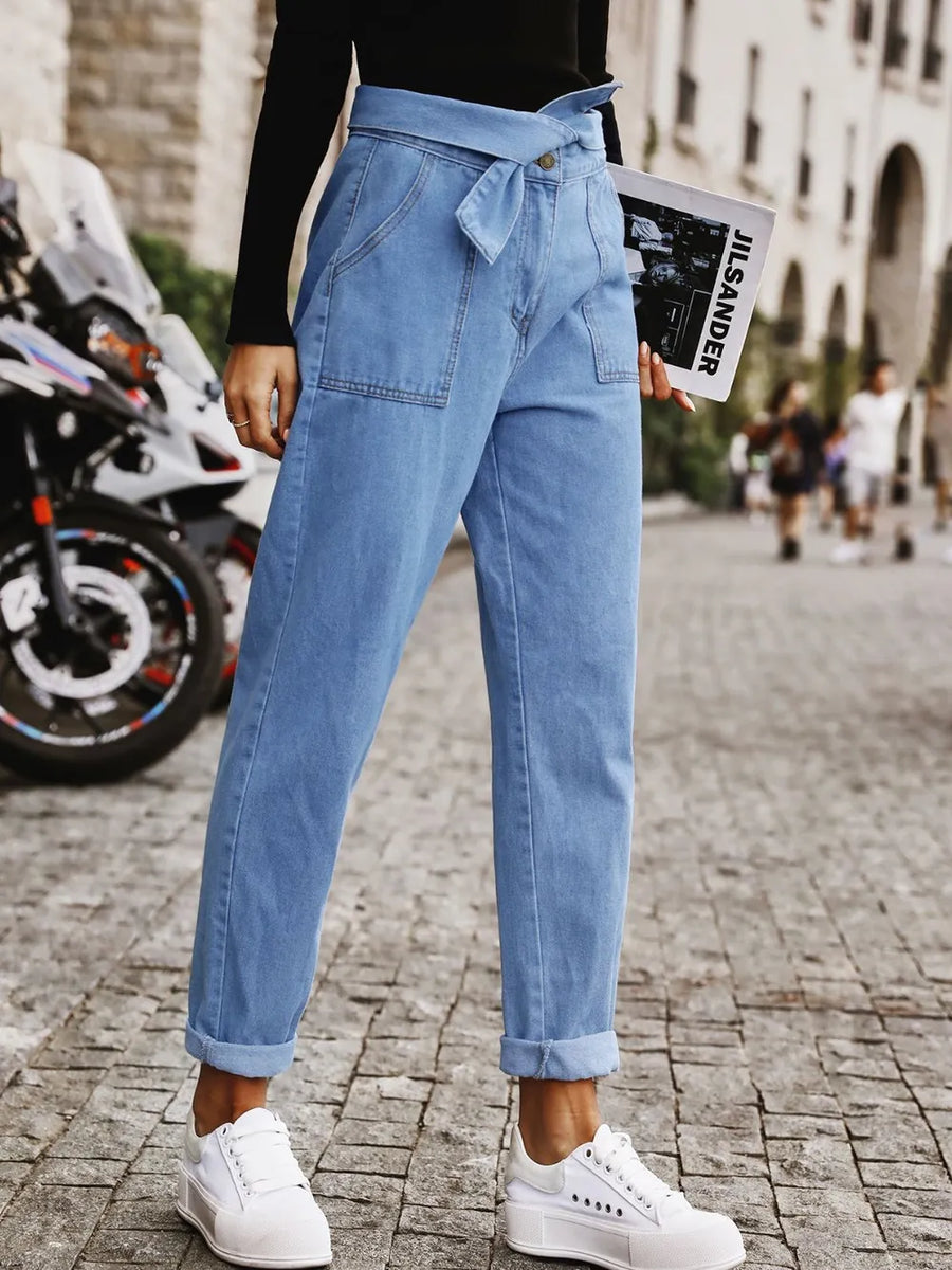 Person wearing blue jeans and white sneakers on a city street.
