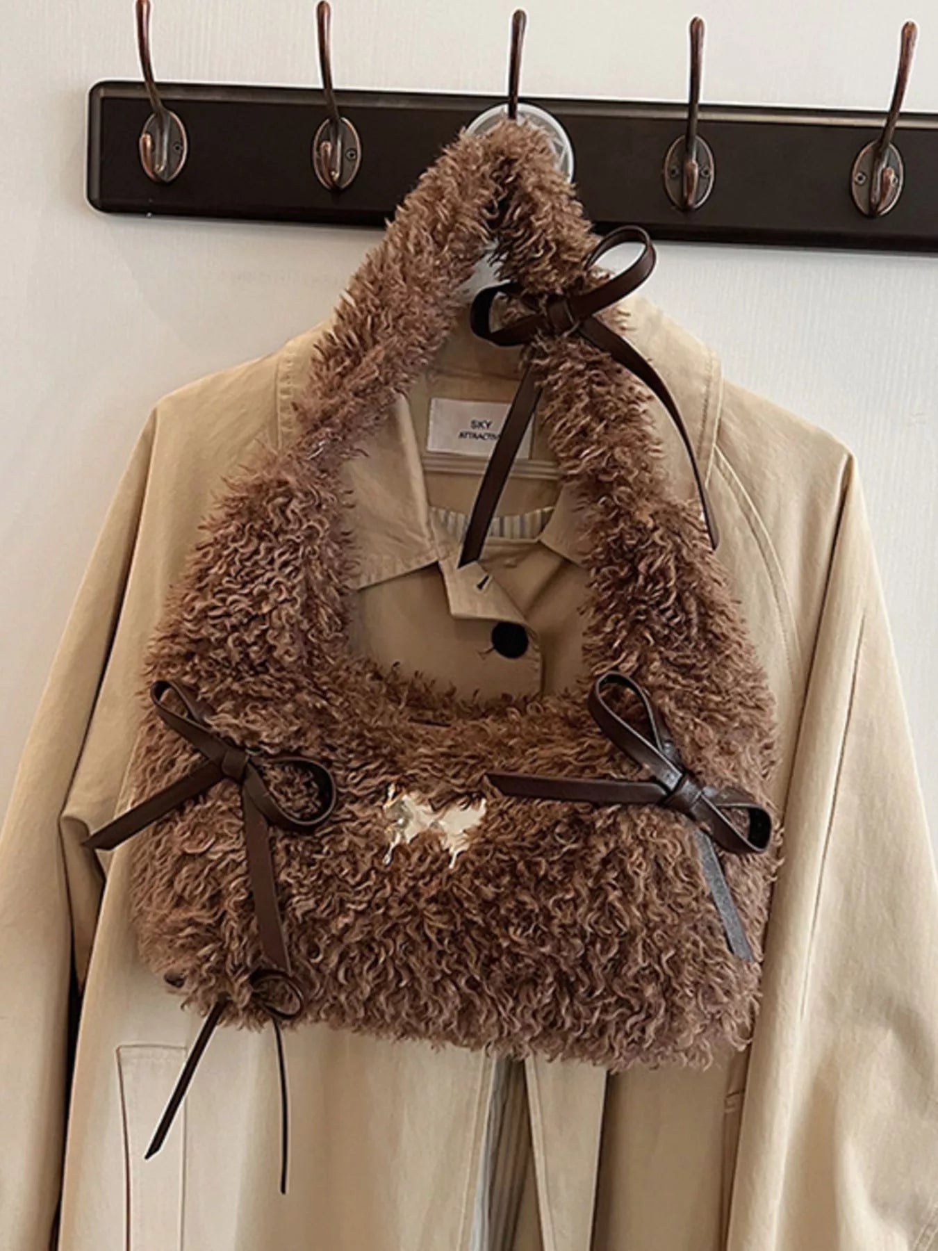 Brown fur vest with a belt over a beige coat on a rack.